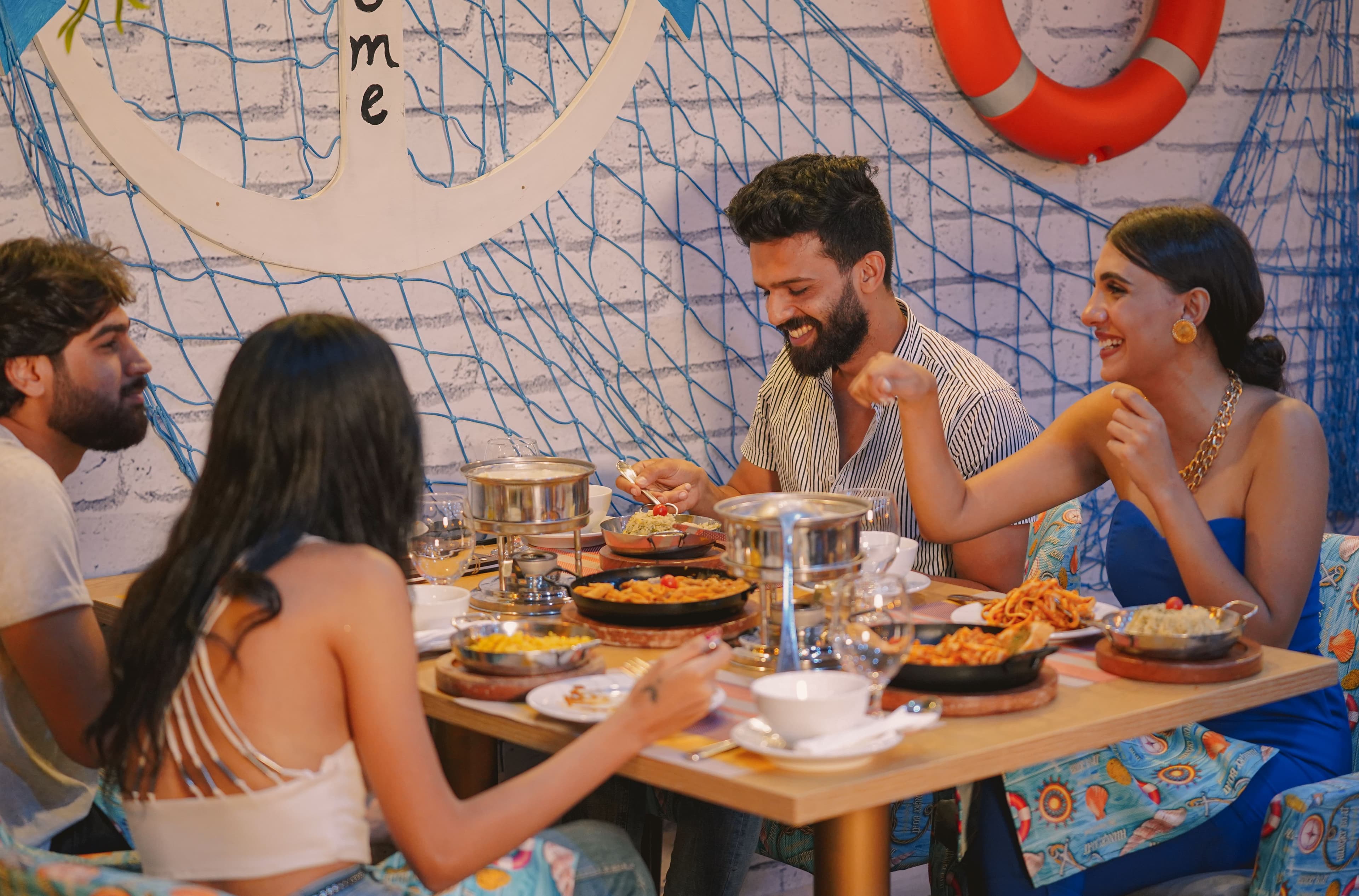 Un grupo de amigos comparte una mesa llena de platos en un restaurante de ambiente marinero
